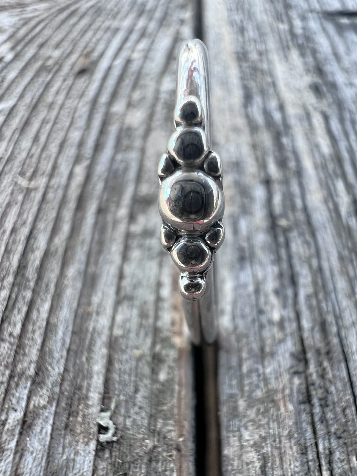 Close-up of a handmade sterling silver granule row ring on driftwood, highlighting the line of fused silver beads