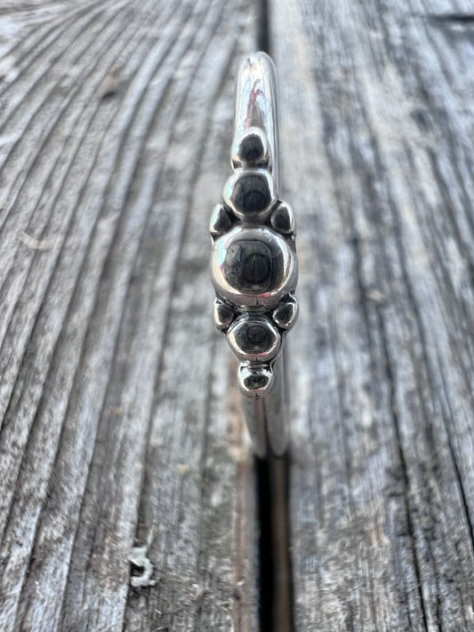 Close-up of a handmade sterling silver granule row ring on driftwood, highlighting the line of fused silver beads
