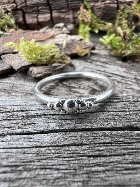Recycled sterling silver granule row ring on driftwood, showing the fine band with a row of silver granule details