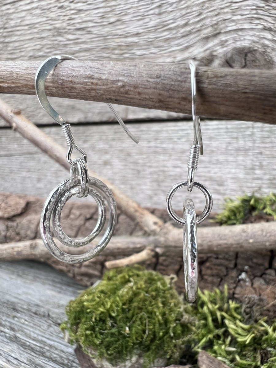 Handmade sterling silver harmonic circles earrings hanging from a branch, photographed from the side showing pendant depth and texture
