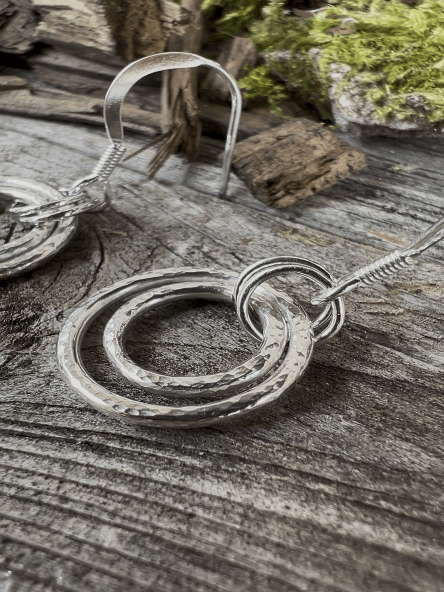 Close-up of handmade sterling silver harmonic circles earrings on weathered wood, highlighting the layered ring pendant and fine wire detail