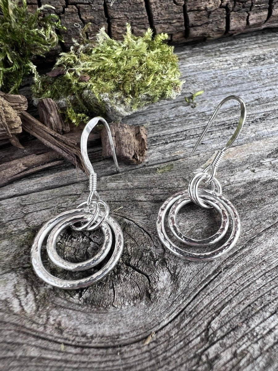 Recycled sterling silver harmonic circles drop earrings on weathered wood, showing the concentric open circle pendant design