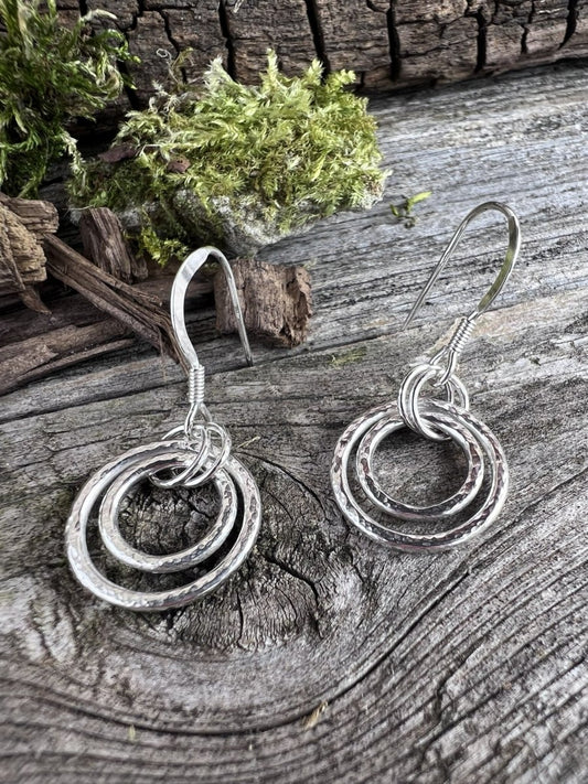 Recycled sterling silver harmonic circles drop earrings on weathered wood, showing the concentric open circle pendant design