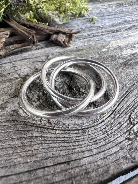 Close-up of handmade sterling silver interlinking rings on a wooden surface, showing how the loops connect