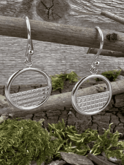 Handmade sterling silver lattice halo earrings hanging from wooden branch, side view showing the halo frame depth
