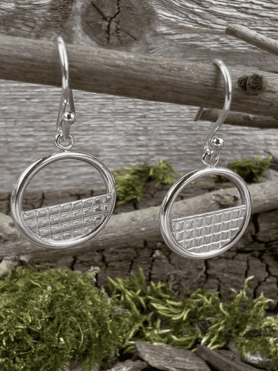 Handmade sterling silver lattice halo earrings hanging from a branch, photographed from the side showing the halo frame depth