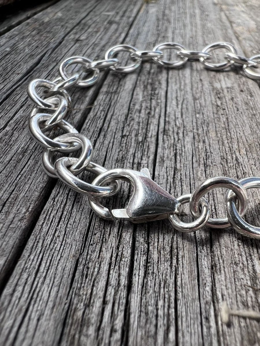 Handmade sterling silver Lina trace bracelet on weathered wood, photographed from an angle showing the lobster clasp detail