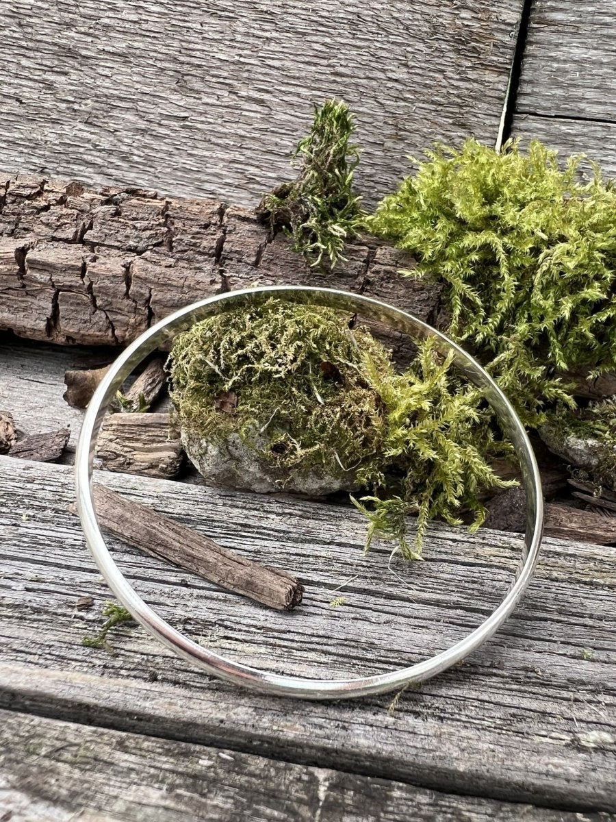 Handmade sterling silver minimal luxe bangle on wood with moss, photographed from the front