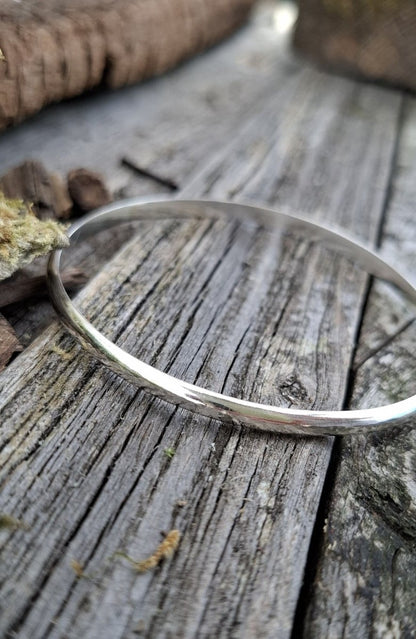 Recycled sterling silver minimal luxe bangle lying on weathered wood, minimalist handmade jewellery