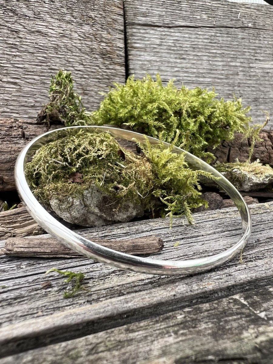 Recycled sterling silver minimal luxe bangle on weathered wood with moss, showing the smooth fine round band