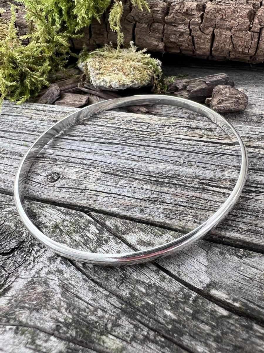 Recycled sterling silver minimal luxe bangle styled on mossy wood, showing the simple circular band