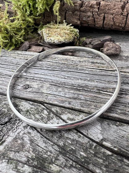 Recycled sterling silver minimal luxe bangle styled on mossy wood, showing the simple circular band