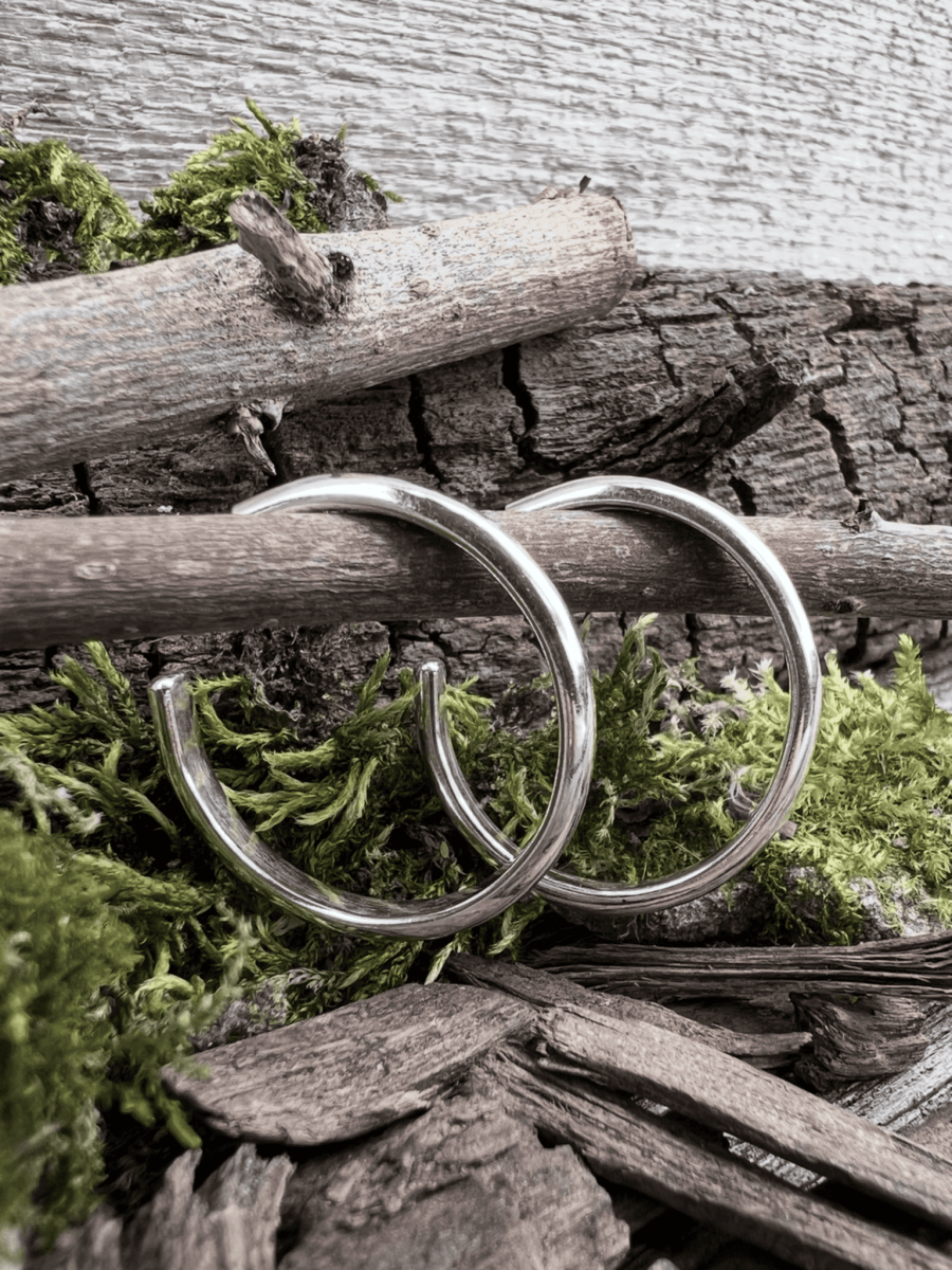 Handmade sterling silver mini hoop medium earrings hanging from a branch with green moss, Isle of Wight jewellery