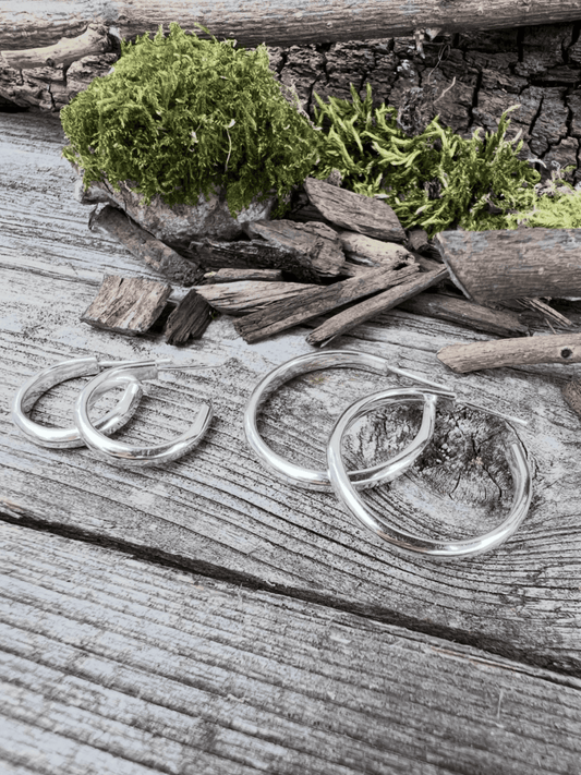 Close-up of handmade sterling silver mini luxe hoop earrings on weathered wood, showing the two sizes side by side