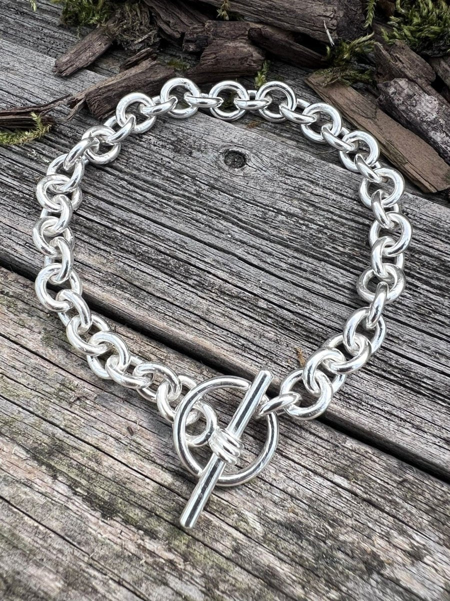 Handmade sterling silver Nova oval loop bracelet on weathered wood, photographed from above showing the full chain and toggle