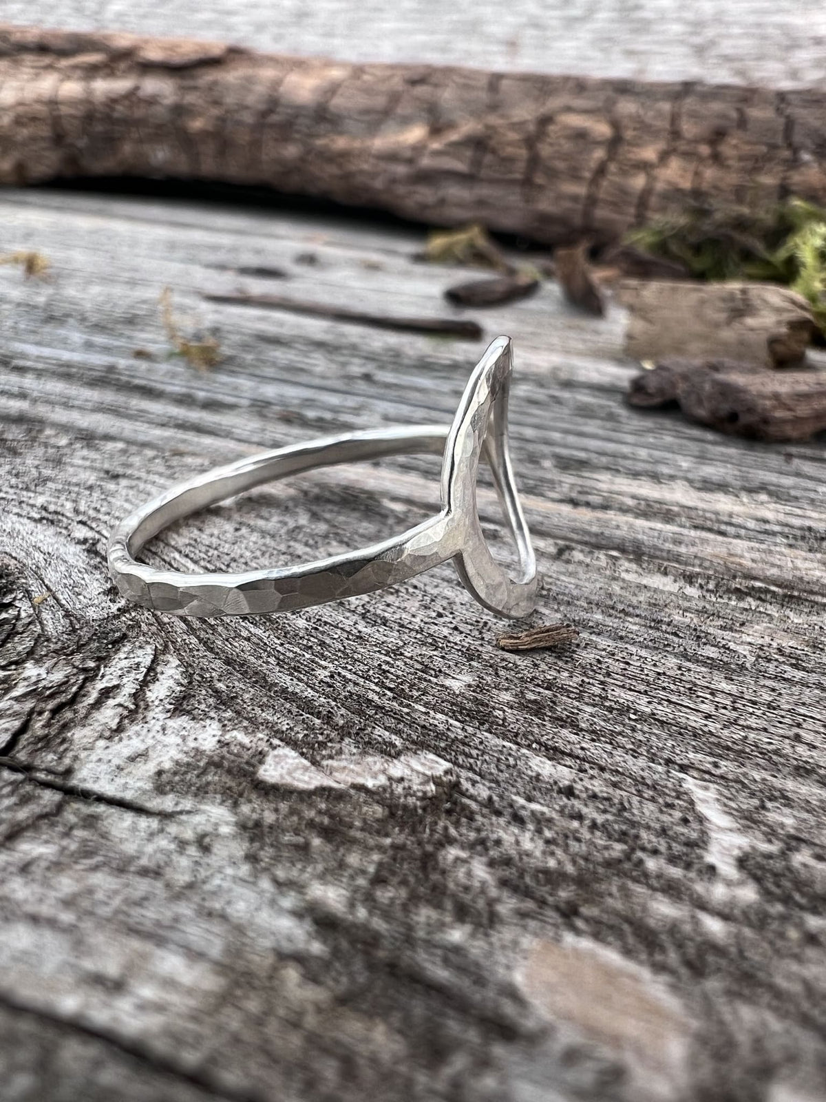 Handmade sterling silver open circle ring on driftwood, side angle showing the open-ended band profile