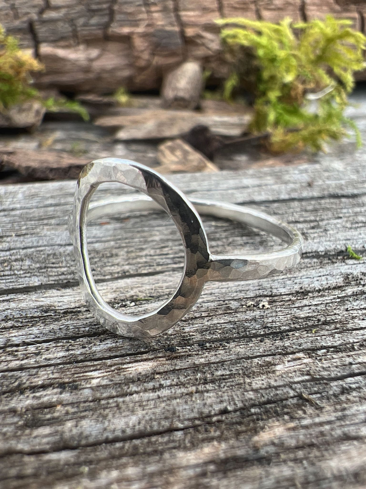 Close-up of a handmade sterling silver open circle ring on driftwood, highlighting the polished oval frame detail