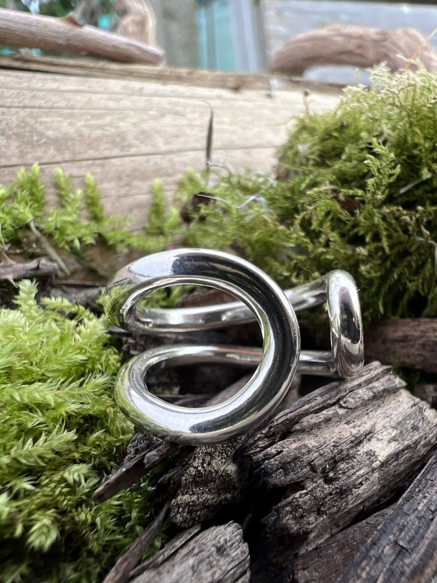 Recycled sterling silver open end loop ring resting on weathered wood chips with green moss in the background