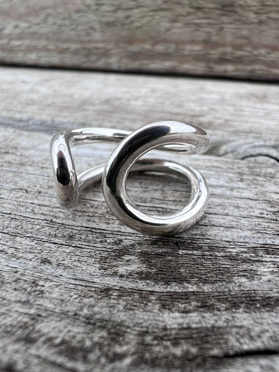 Close-up of a handmade sterling silver open loop ring showing the curved wire ends and polished finish on a wooden surface
