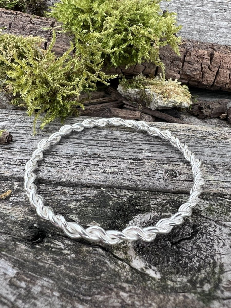 Handmade sterling silver open twist bangle on mossy wood, photographed from overhead showing the twist detail
