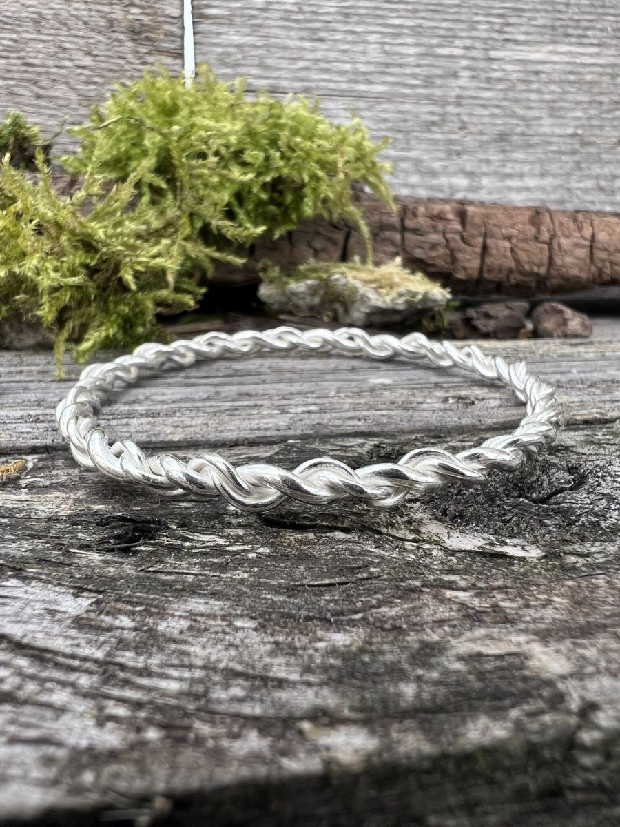Recycled sterling silver open twist bangle lying on mossy wood, handmade Isle of Wight jewellery