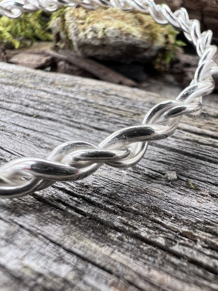 Close-up of a handmade sterling silver open twist bangle on wood, highlighting the twisted texture