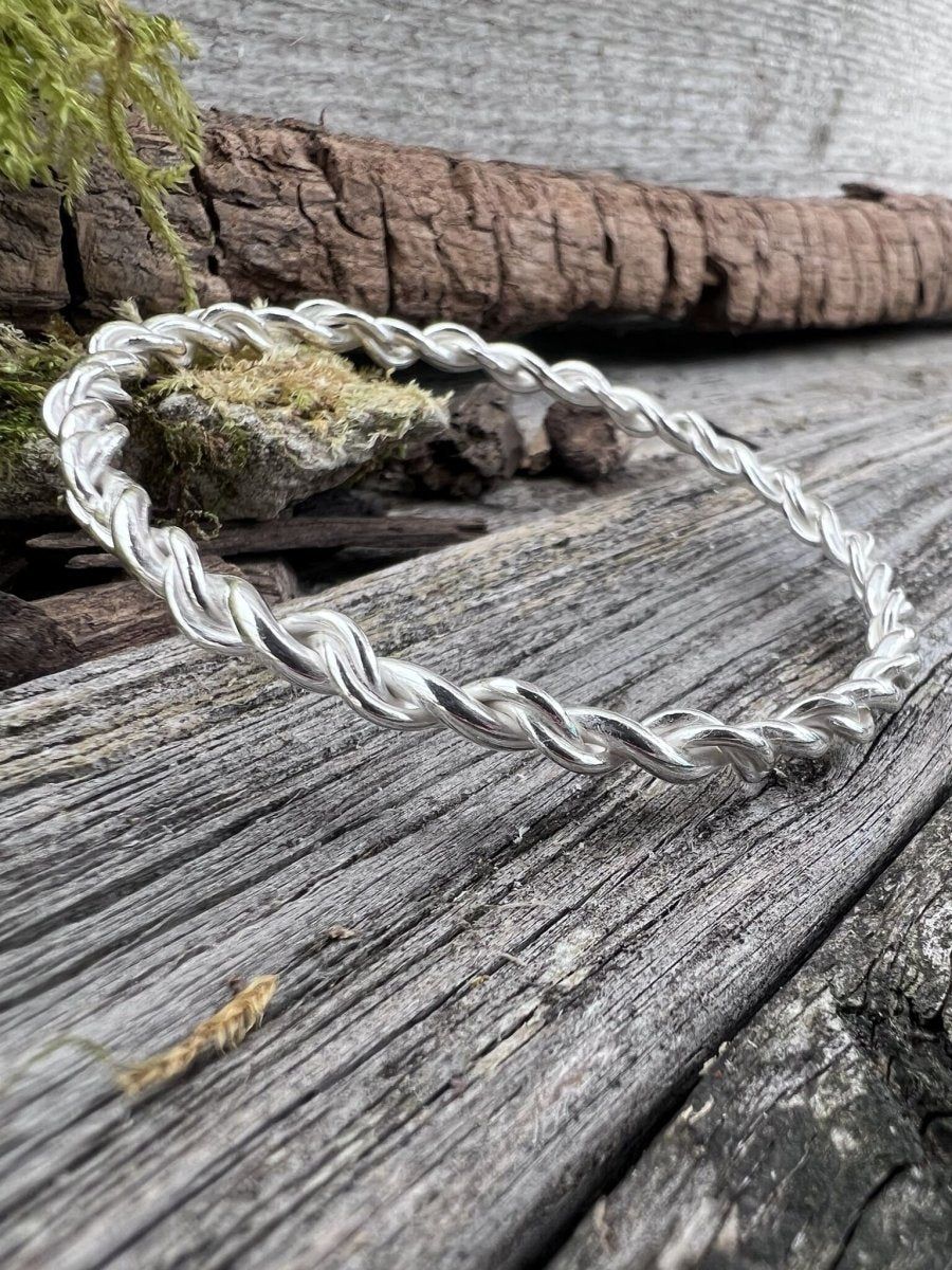 Recycled sterling silver open twist bangle on weathered wood with moss, showing the twisted band