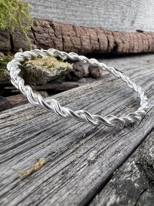 Recycled sterling silver open twist bangle on weathered wood with moss, showing the twisted band