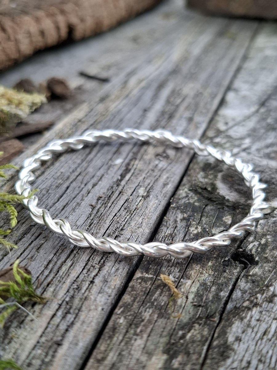 Recycled sterling silver open twist bangle styled on weathered wood, showing the full twisted circular form