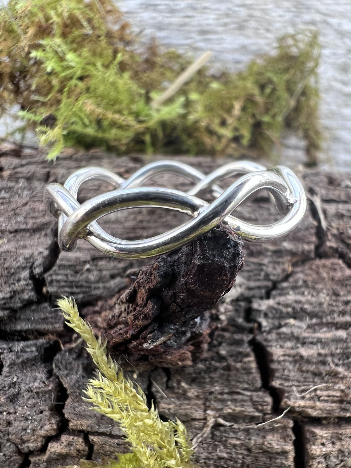 Handmade sterling silver open twist ring on mossy driftwood, angled view showing the layered wire twist form