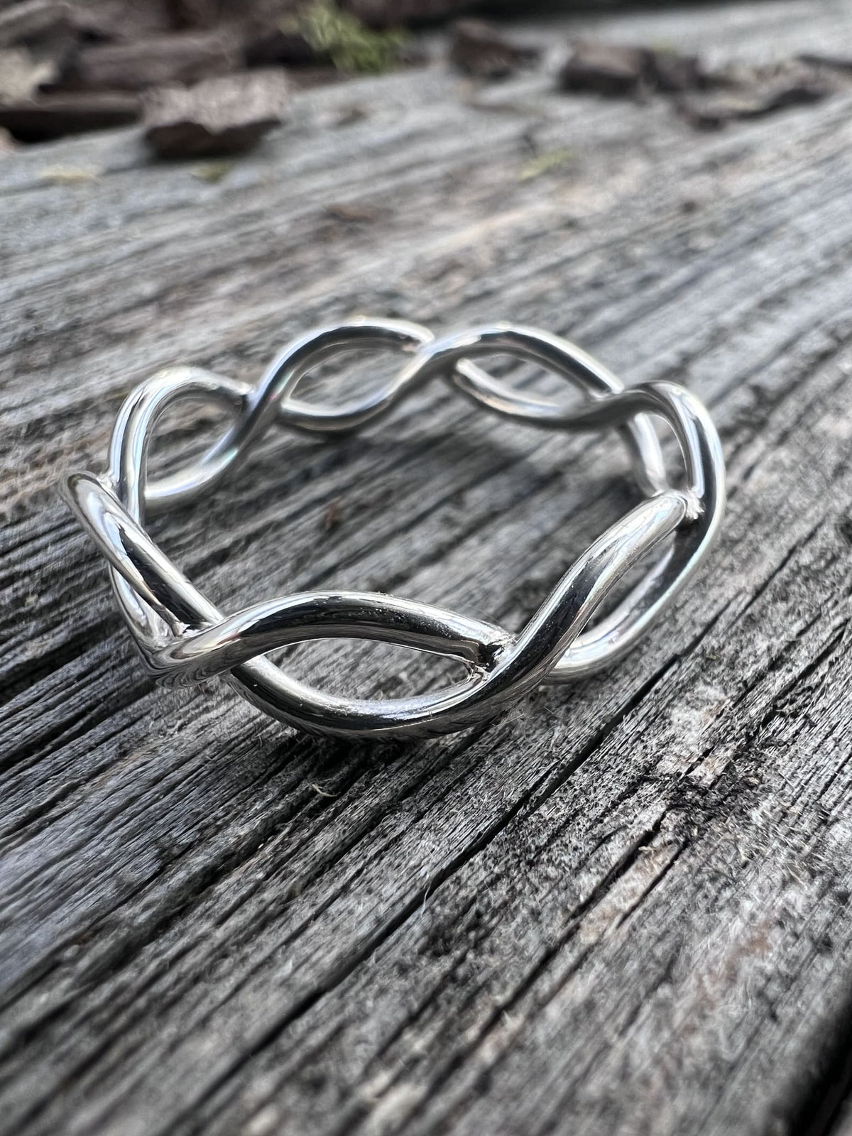 Close-up of a handmade sterling silver open twist ring on driftwood, highlighting the interlaced wire twist detail
