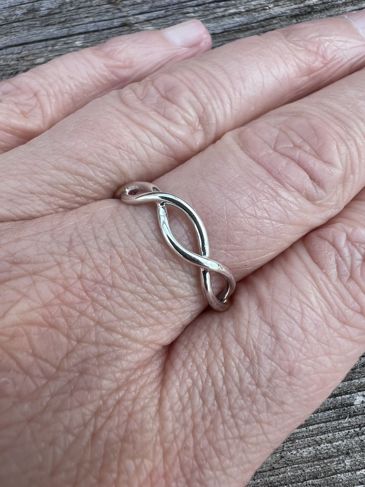 Sterling silver open twist ring worn on a finger, showing scale and the interwoven open twist band