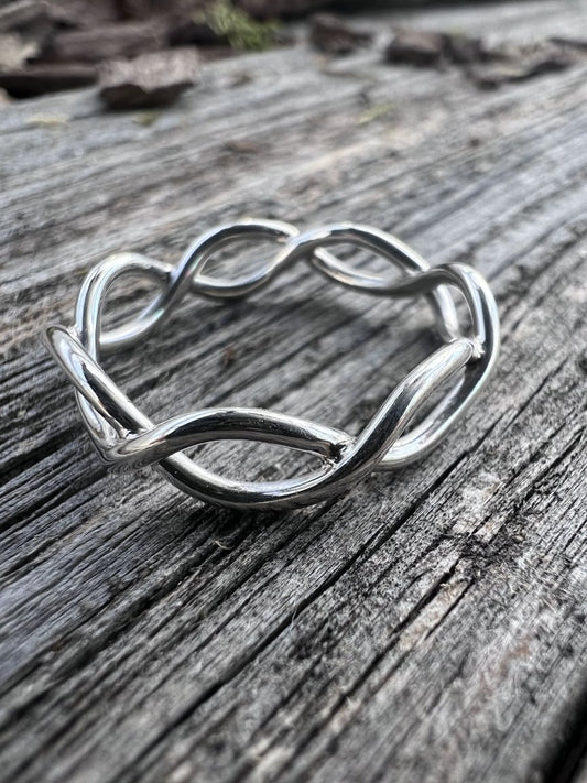 Close-up of a handmade sterling silver open twist ring on driftwood, highlighting the interlaced wire twist detail