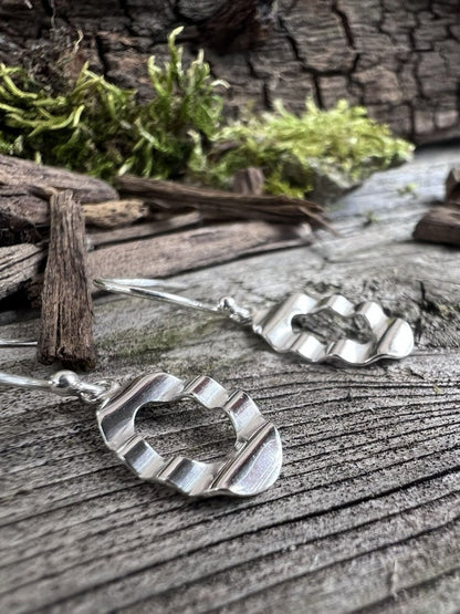 Recycled sterling silver oval wave drop earrings on wooden surface with moss, showing the undulating open oval pendant