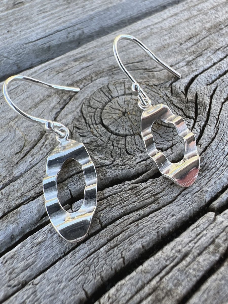 Close-up of handmade sterling silver oval wave earrings on weathered wood, highlighting the wavy cut out oval shape
