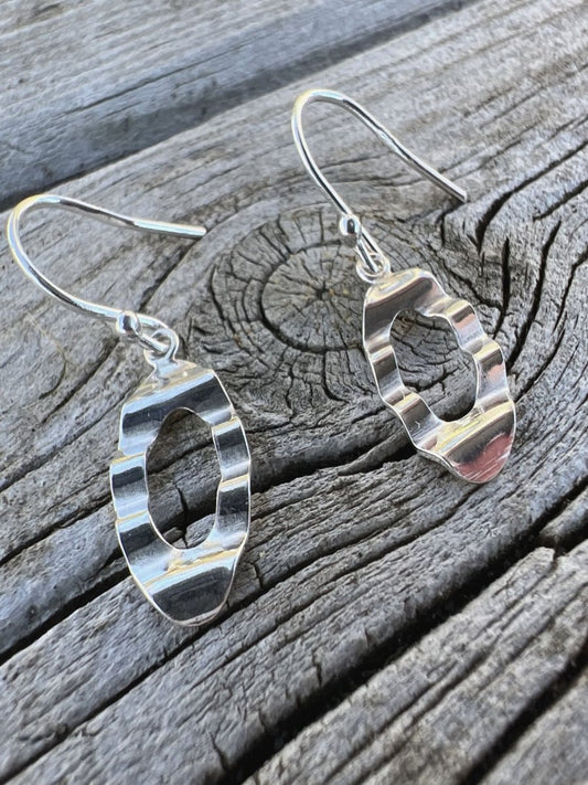 Close-up of handmade sterling silver oval wave earrings on weathered wood, highlighting the wavy cut out oval shape