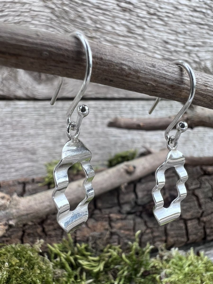 Recycled silver oval wave drop earrings hanging from a branch showing the side profile of the wave design