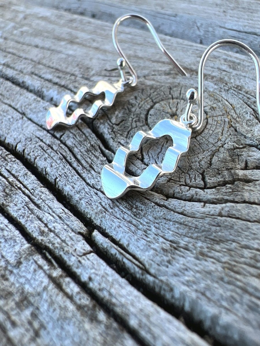 Handmade sterling silver oval wave earrings on weathered wood viewed from above, showing the wavy outline detail
