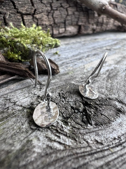 Close-up of handmade sterling silver petite textured oval earrings on weathered wood, showing the fine hammered surface