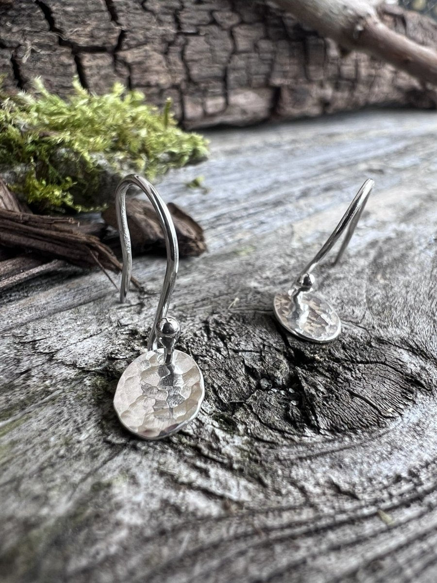 Close-up of handmade sterling silver petite textured oval earrings on weathered wood, highlighting the fine hammered surface and small scale