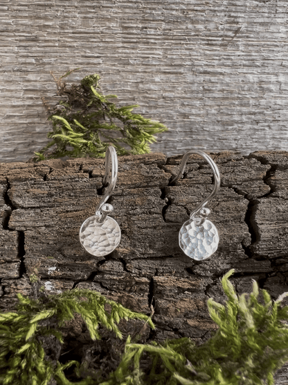 Recycled silver petite textured oval earrings styled on a bark background with foliage, showing the tiny pendant