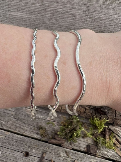 Recycled sterling silver wave bangles stacked on a wrist, showing how the wave shapes layer together