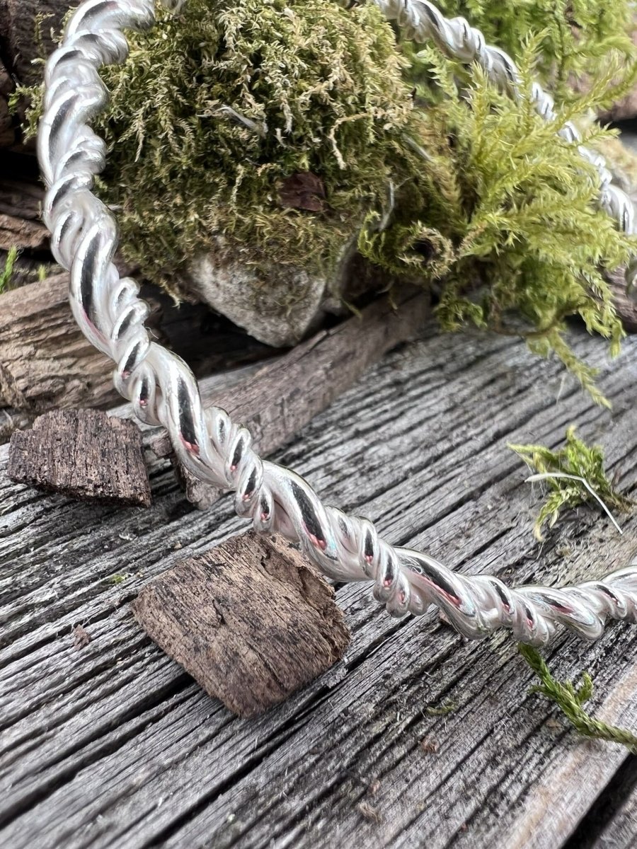 Handmade sterling silver rope twist bangle on mossy wood, photographed from an angle showing the twist pattern