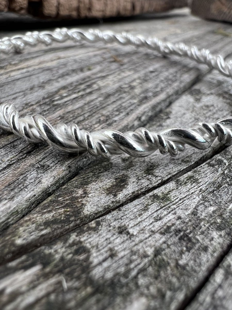 Close-up of a handmade sterling silver rope twist bangle on wood, highlighting the twisted wire texture