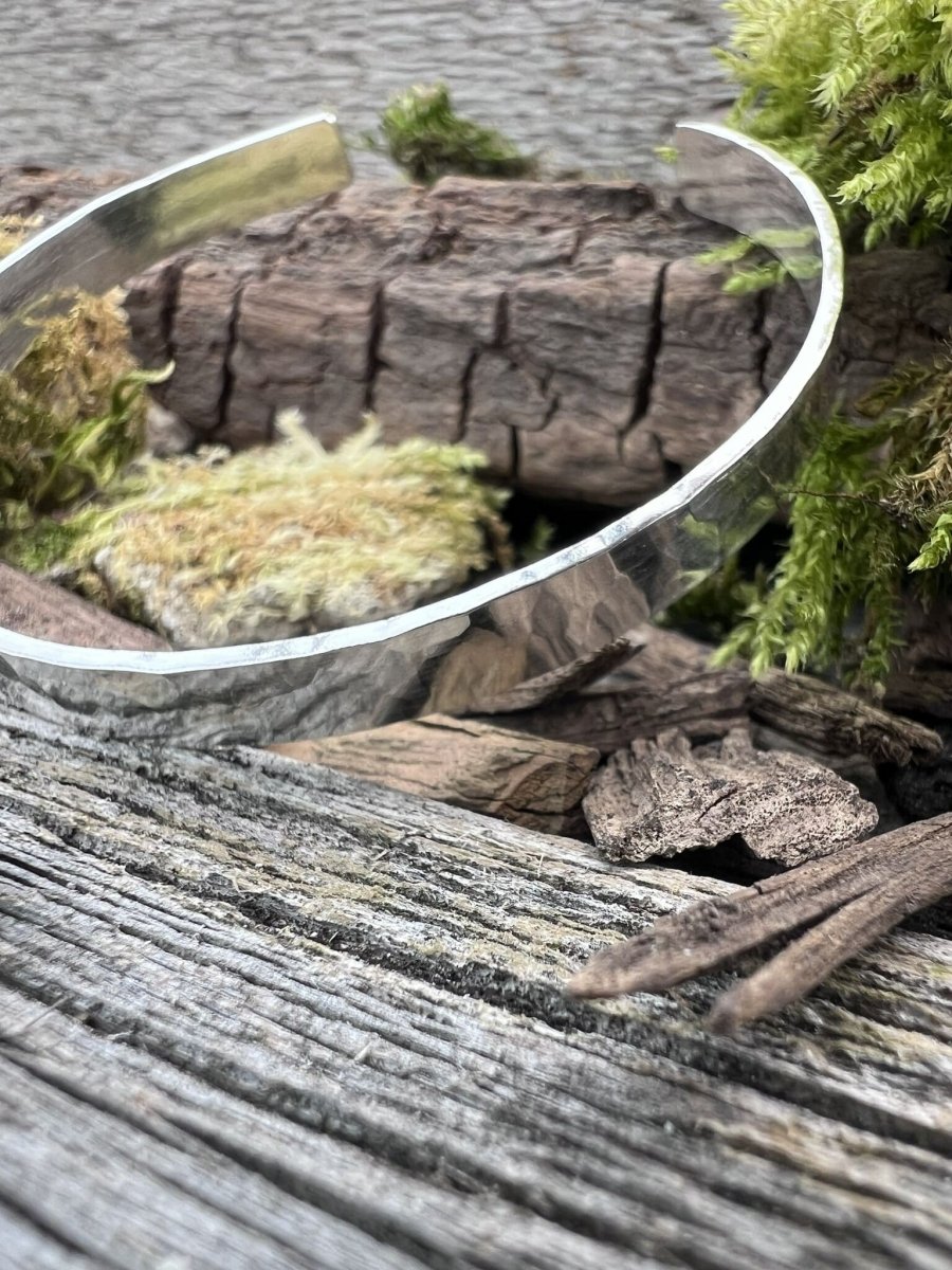 Handmade sterling silver Sierra textured torque bangle on weathered wood with moss and bark, photographed from an angle