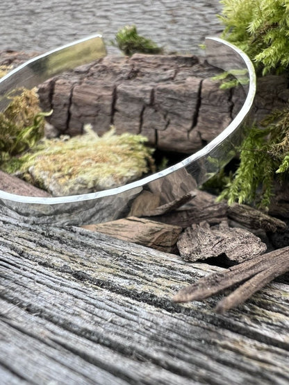 Handmade sterling silver Sierra textured torque bangle on weathered wood with moss and bark, photographed from an angle