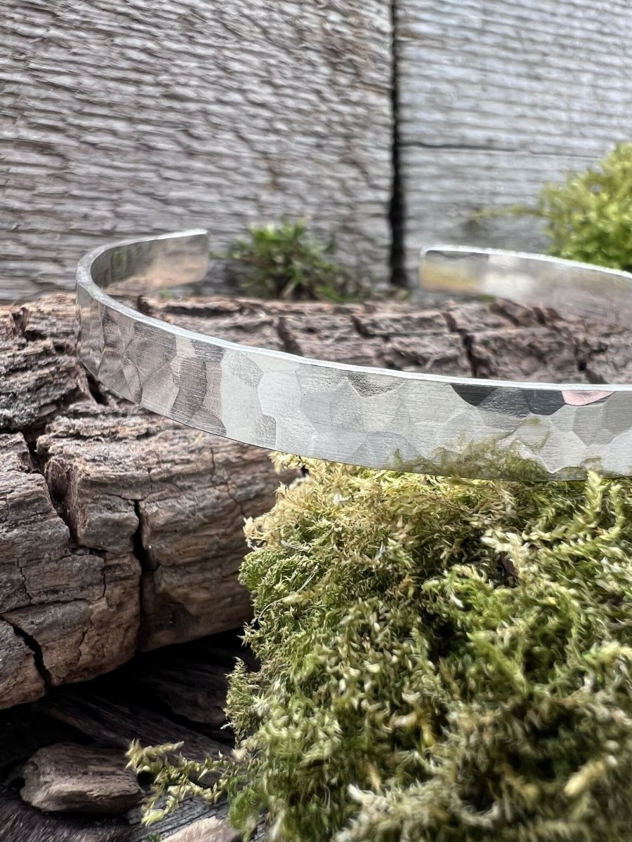 Close-up of a handmade sterling silver Sierra textured torque bangle on weathered wood, showing the textured pattern