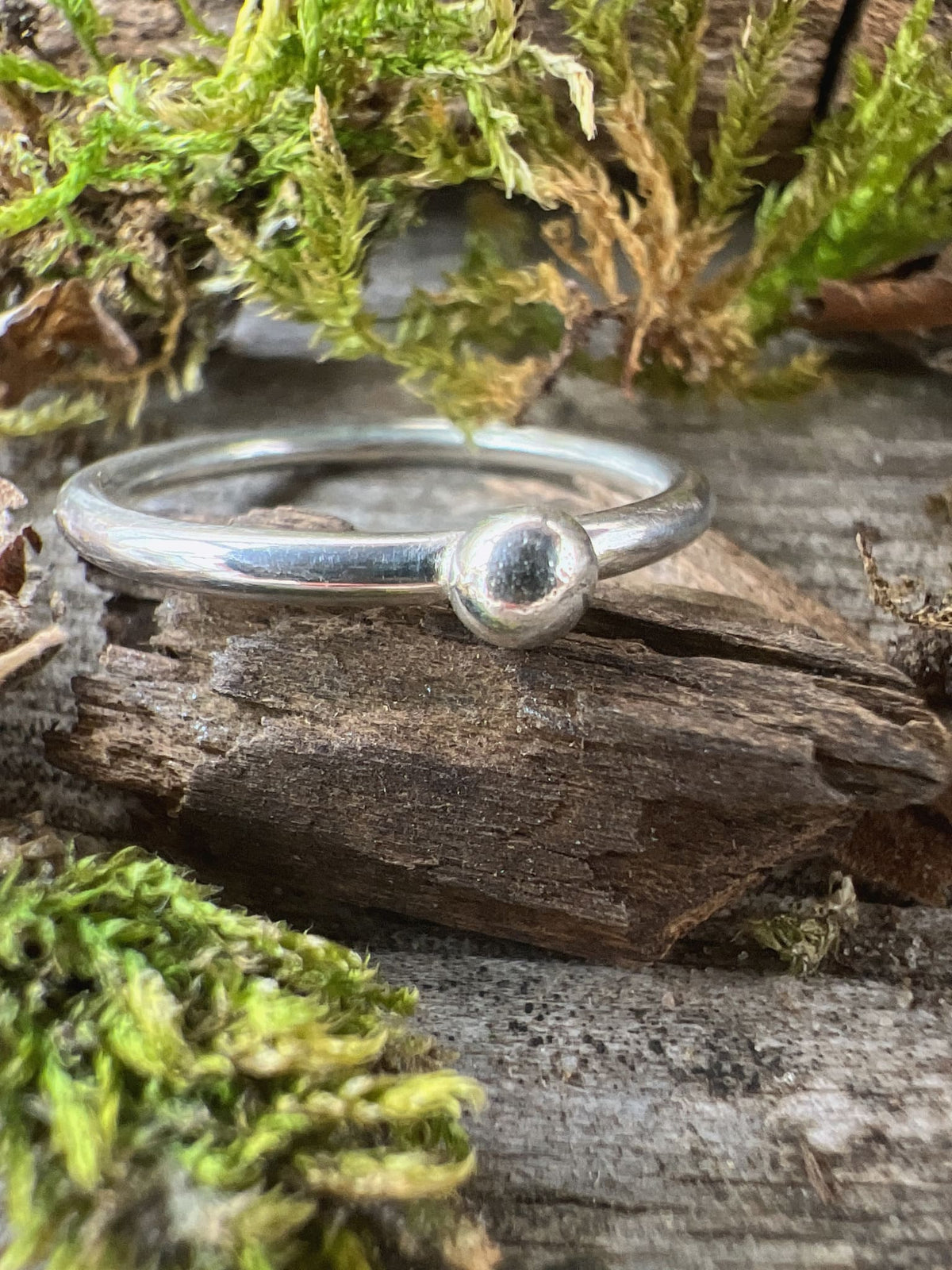Handmade sterling silver single granule ring on mossy driftwood, angled view showing the single silver bead