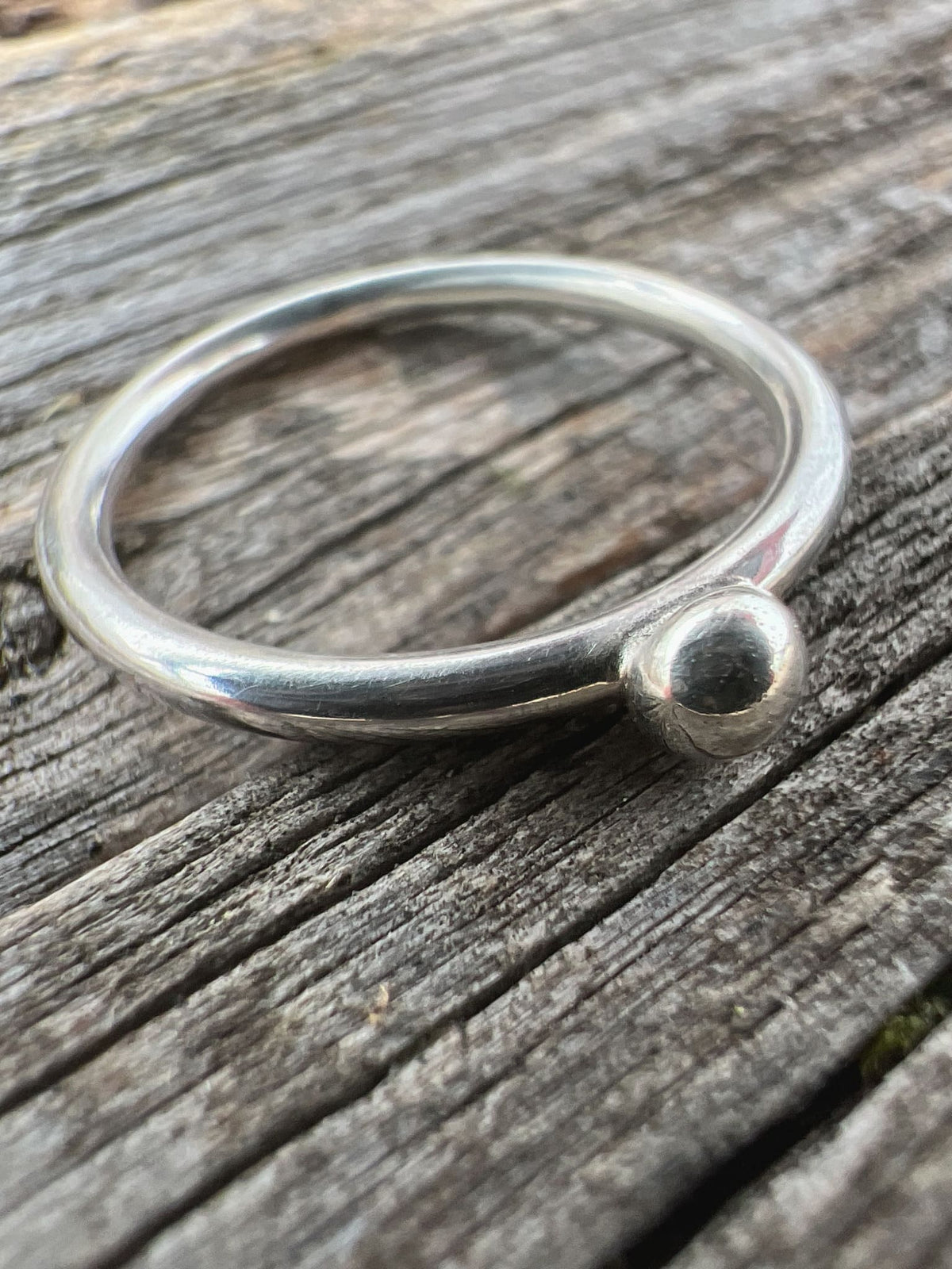 Close-up of a handmade sterling silver single granule ring on driftwood, highlighting the solitary fused silver bead