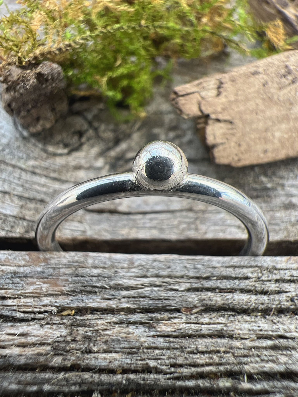 Handmade sterling silver single granule ring on driftwood, overhead view showing the single bead from above